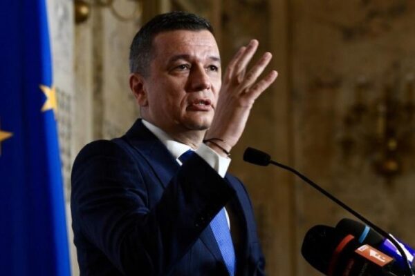 Bărbat ținând discurs la pupitru, steag UE